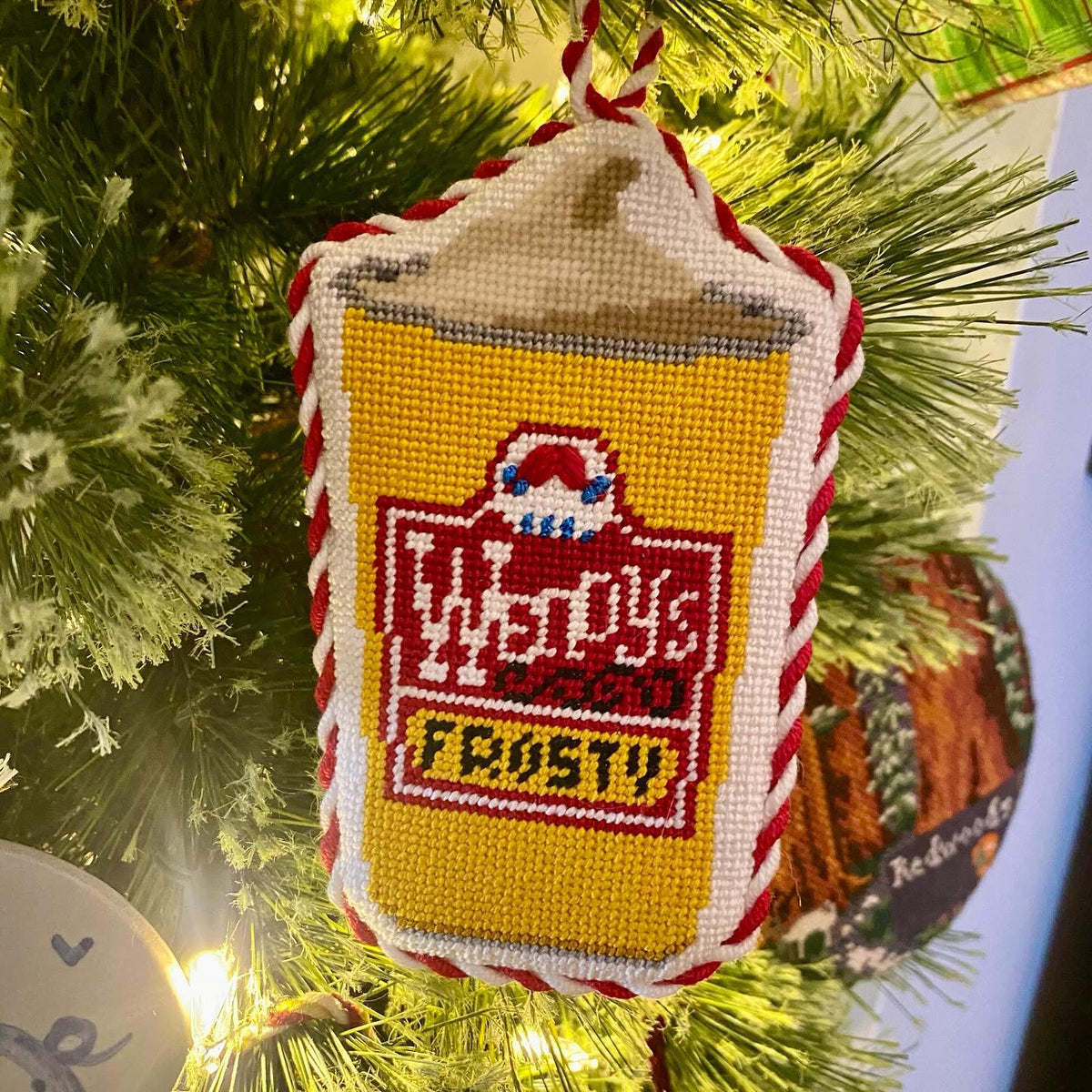 Finished Frosty needlepoint ornament hanging on a lit Christmas tree from @pinpointneedlepoint on Instagram